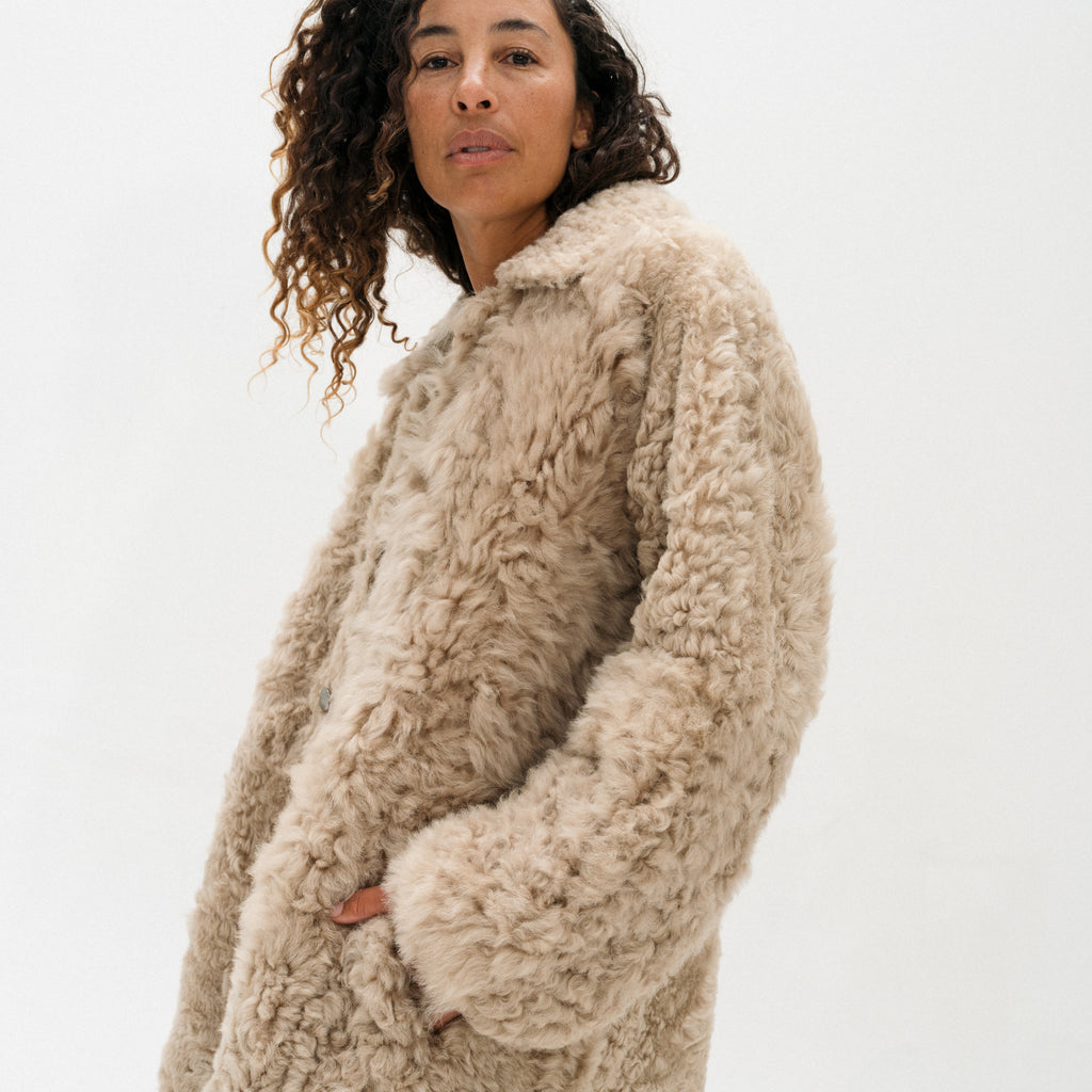 A woman wearing a chunky, textured beige sherpa fleece coat, photographed against a clean white studio background.