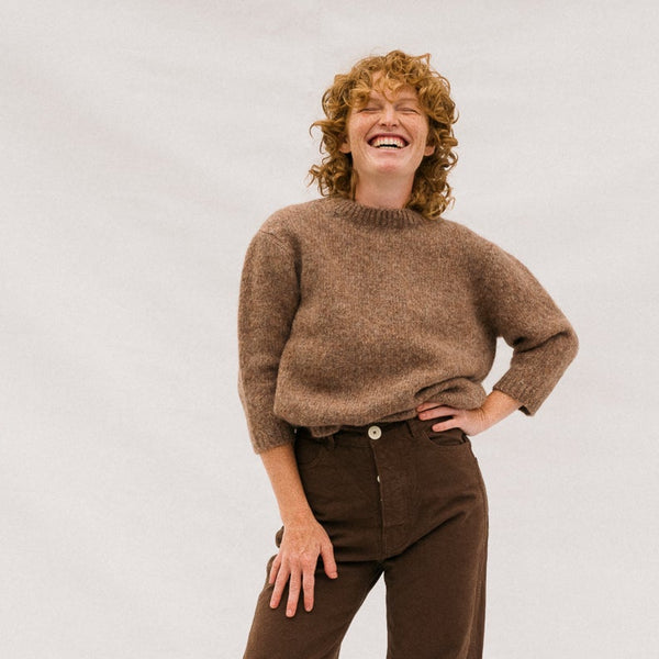 Person wearing a brown sweater and pants on a white background
