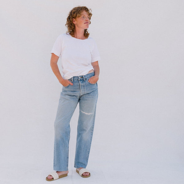 Person wearing a white t-shirt and light blue jeans standing against a plain background