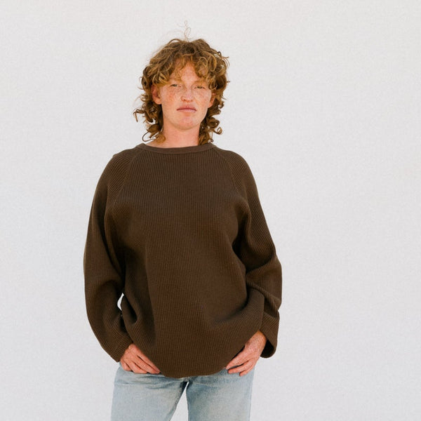 Person wearing a brown sweater and light blue jeans on a white background