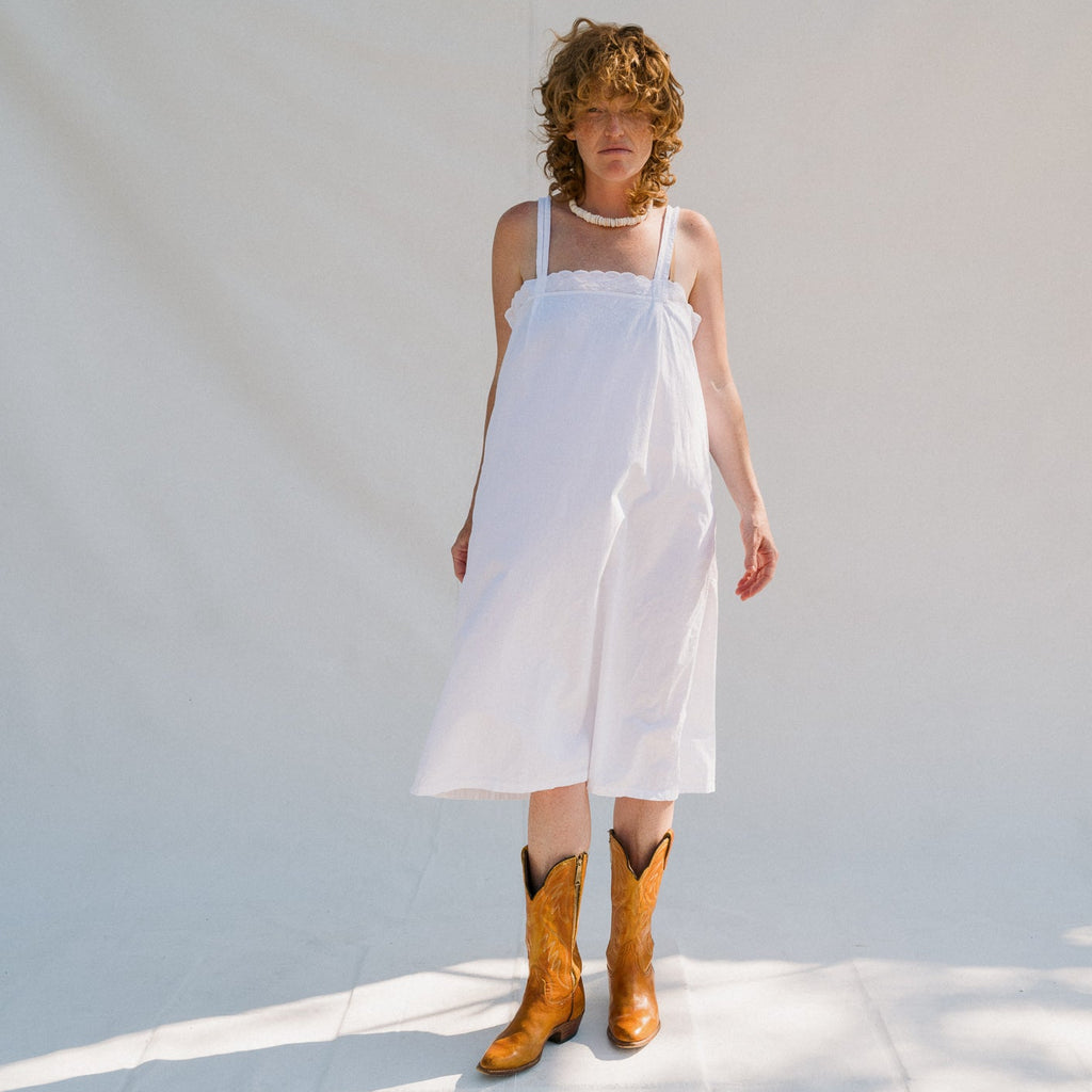 Woman wearing a white dress and brown cowboy boots against a light background