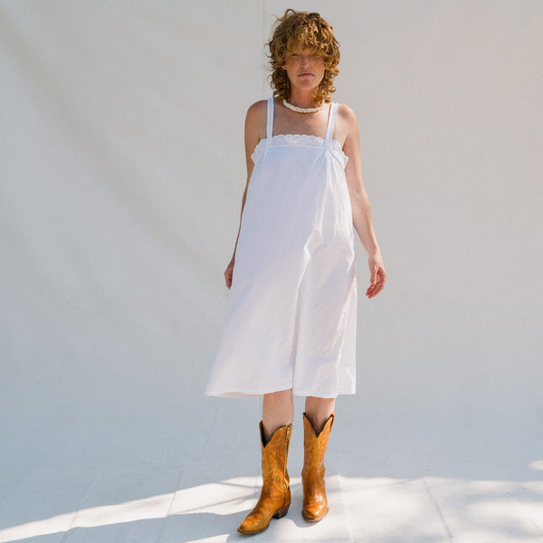Woman wearing a white dress and brown cowboy boots against a light background